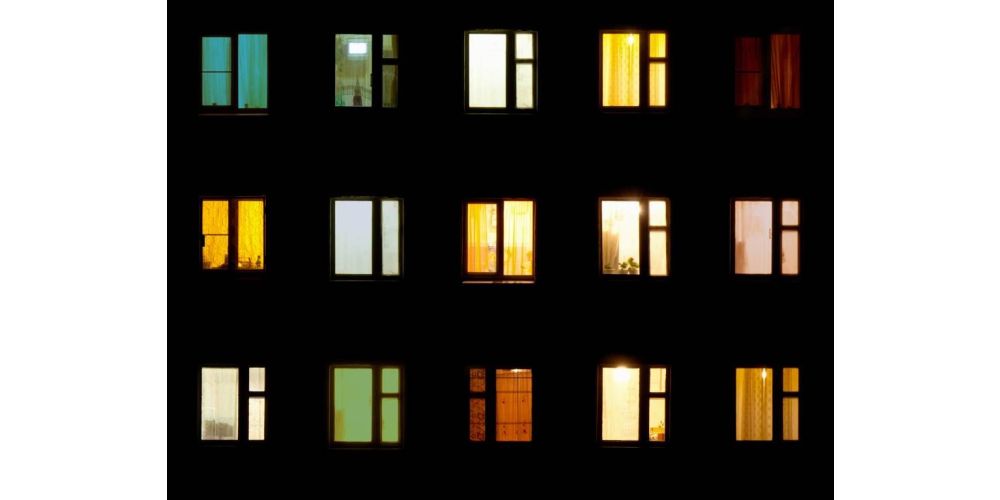 A multi-colored array of apartment building windows aglow at night