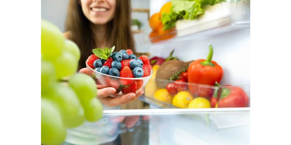 A woman removes a bowl of fruit from a stocked refrigerator