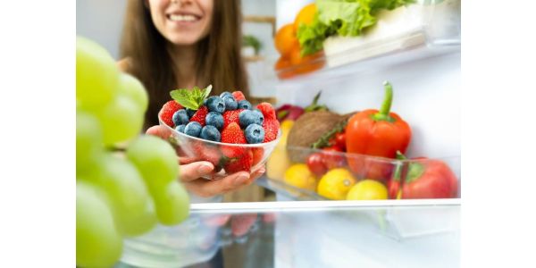 A woman removes a bowl of fruit from a stocked refrigerator