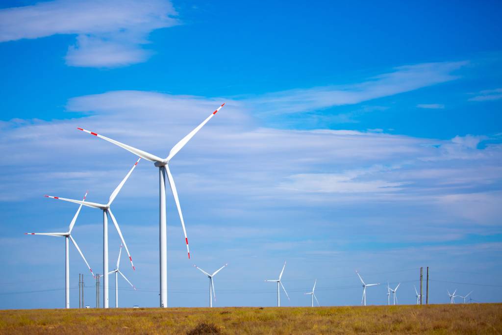 A fleet of wind turbines against a bright blue sky