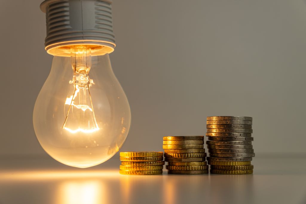 An illuminated lightbulb beside three small stacks of coins